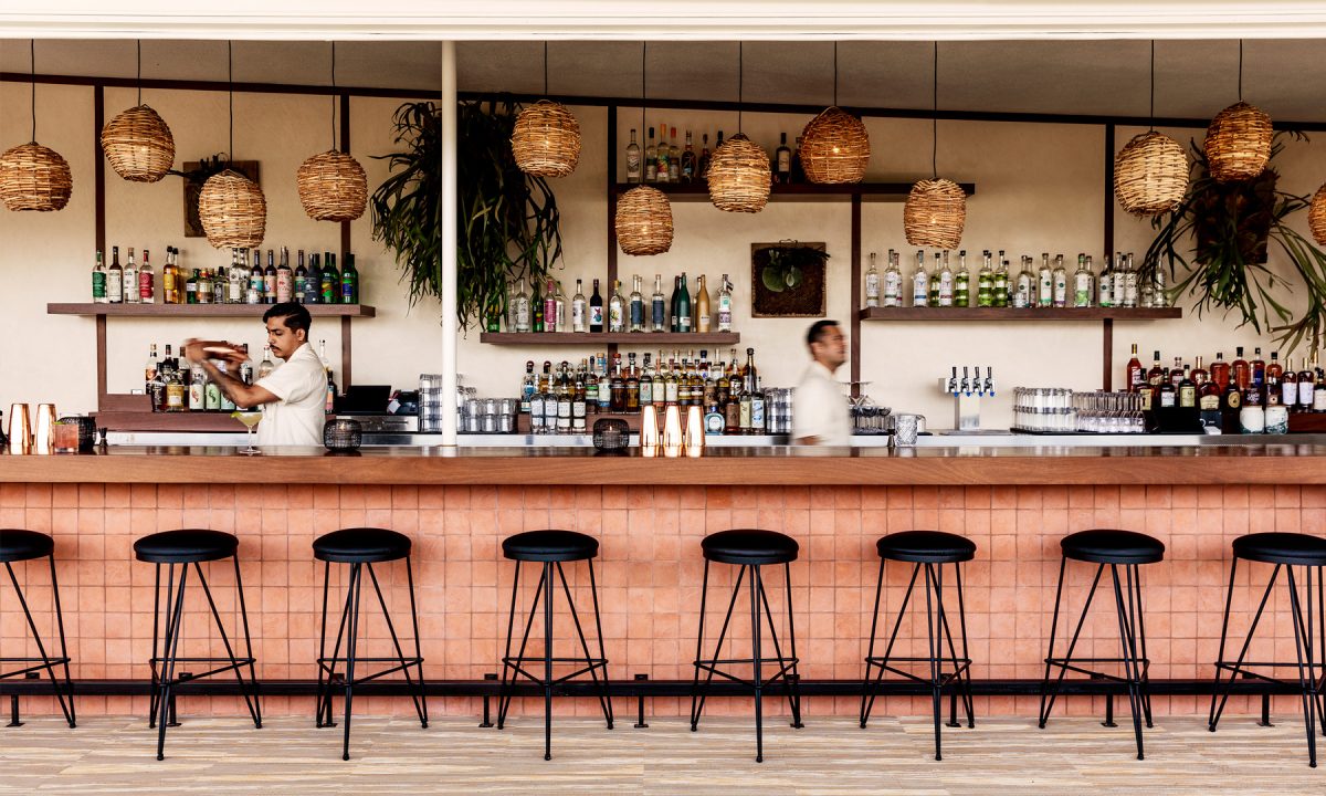 Long bar with stools and bartenders working in front of various liquor bottles