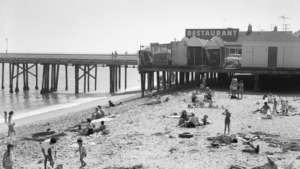old black and white image of beach goers enjoying the ocean next to Malibu Pier