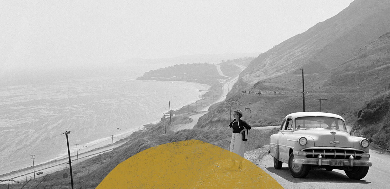 Black and white image of woman looking out of her car at the view of pacific coast highway
